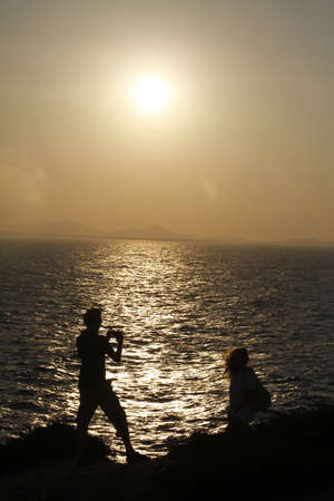 A vertical shot of a male taking a picture of his girlfriend by the ocean captured at sunset