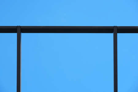 A low angle shot of a black metal roof railing on a blue sky background