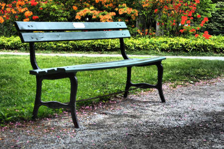 A closeup of a wooden bench with metal legs in a park on a summer dayの写真素材