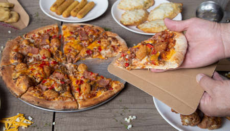 A closeup shot of a male hand grabbing a slice of meat pizza