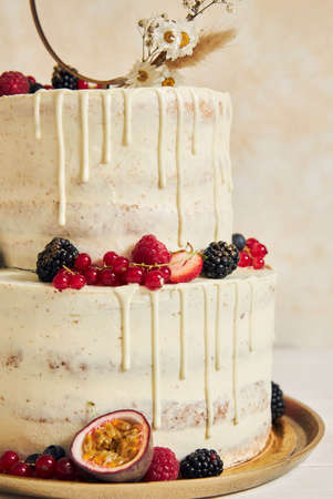A vertical shot of a wedding cake decorated with fresh fruits and berries and a flower ring