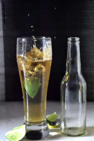 A vertical shot of a drop of lime with a splash of cold beer and a bottle on the side