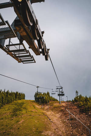 A vertical shot of chairlifts surrounded by greenery under a cloudy skyの写真素材