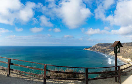 A landscape of the sea surrounded by hills under a blue cloudy sky and sunlightの写真素材