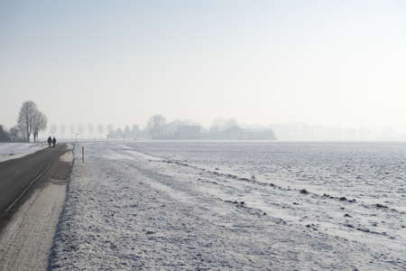 Two people walking by the lake surrounded by trees in the early morning