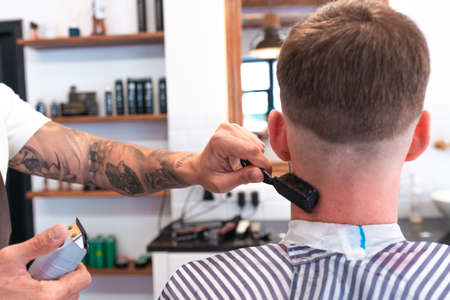 A closeup of a hairdresser with tattoos cleaning the male customer's neck with a brushの写真素材