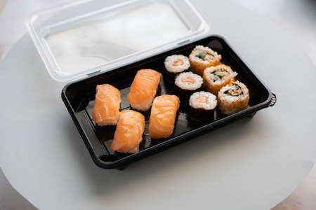 A closeup shot of delicious sushi rolls in a plastic box on a white surfaceの写真素材