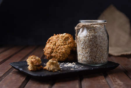 A selective focus shot of a black plate with oat cookies and a glass jar with uncooked oats on a wooden surfaceの写真素材