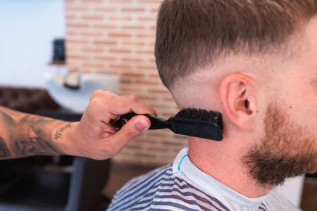A closeup of a hairdresser with tattoos cleaning the male customer's neck with a brushの写真素材