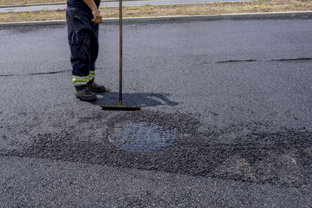 A person cleaning the road after laying down asphalt under the sunlight