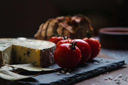 A closeup shot of tomatoes next to bay leaves, bread and blue cheeseの写真素材