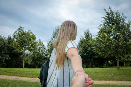 A closeup shot of a male holding a blonde female's hand with trees on the backgroundの写真素材