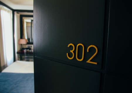 A close shot of a 302 number on a hotel room door with a blurred interior in the backgroundの写真素材