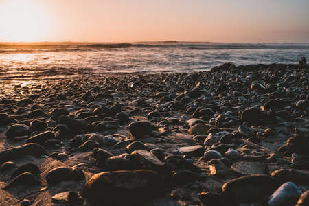 Beach rocks washed up by the waves of the ocean with sunset sky in the background
