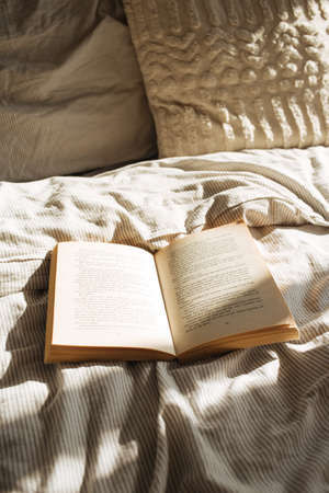 A close up shot of a vintage book on bed sheets under the morning sunshineの写真素材