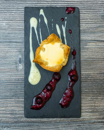 A vertical shot of a desert  with creams on a black tray on a wooden surface