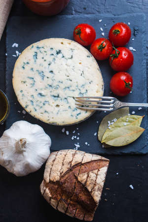 A vertical shot of the blue cheese next to fork, tomatoes, garlic, bread and bay leafの写真素材