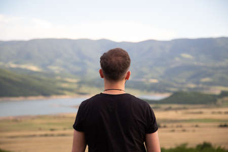 A male in a black t-shirt standing in front of beautiful fields and hills in natureの写真素材