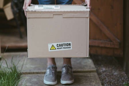 A person holding a cardboard box with a label caution heavy package  on it