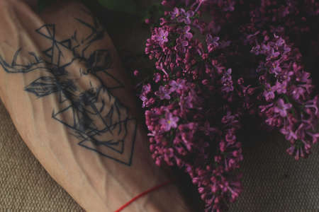 A deer tattoo on a forearm with a red ribbon next to a lilac flower