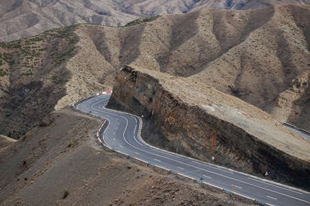 A curvy road around the cliff with mountains in the backgroundの写真素材