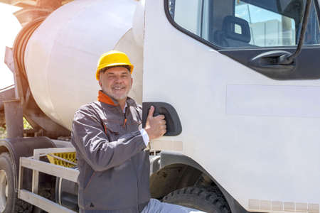 A happy male construction worker doing the thumbs-up gesture in front of a truck under the sunlight