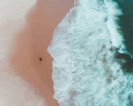 An overhead shot of a male walking on the beach alongside beautiful ocean waves hitting the coastの写真素材