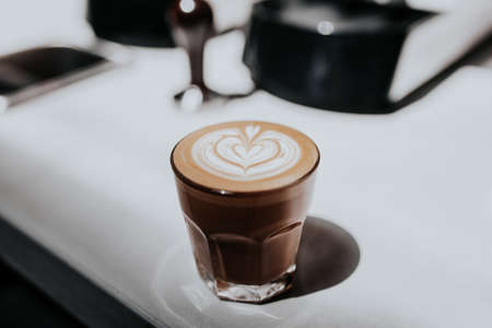 A closeup of a beautifully made cappuccino in a glass cup on a white tableの写真素材