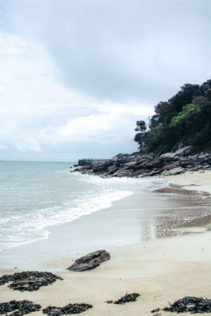 A vertical shot of a beautiful empty beach with cliffs and greenery on the side and amazing cloudy...