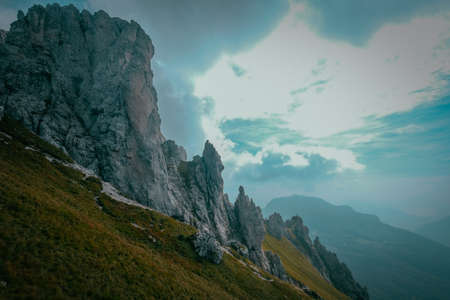 A grassy hill with rocky cliff and mountain with blue sky in the background