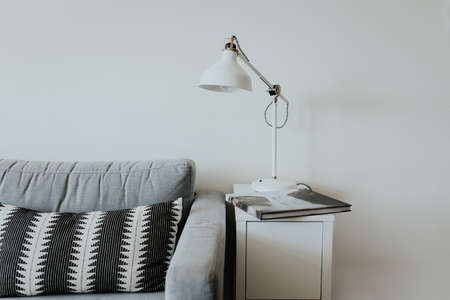 A comfortable couch in modern house with a lamp on a little white shelf and a book with a waterfall...