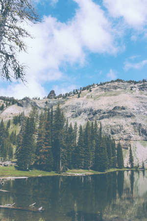 A beautiful lake in a forest with pine trees and reflections in the water next to a rocky hillの写真素材