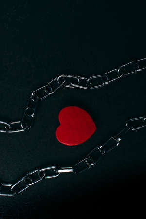 A high angle shot of a wooden red heart and metal chains on a black surfaceの写真素材