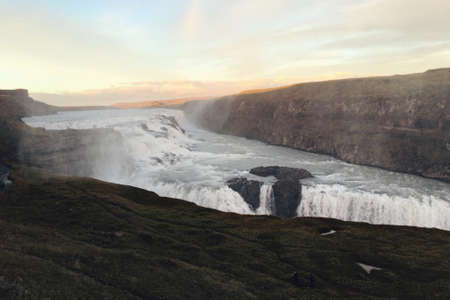 A beautiful shot of a river with a waterfall and hills with a sunny sky in the background