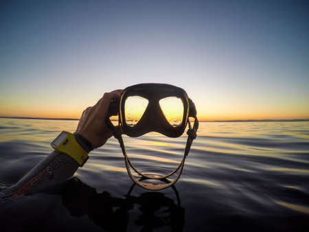 A closeup shot of a diver holding a diving mask on the background of the sea during sunset