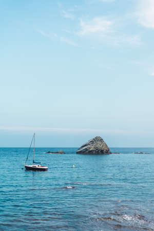 Small sailboat in the sea with a large rock behind on the Costa Brava, Spain