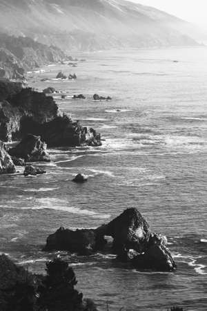 A grayscale vertical shot of sea surrounded by rocks