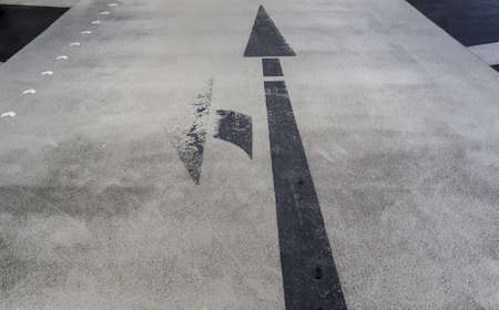 A closeup of black left turn and straight arrow sign on an old small road in northern Europe