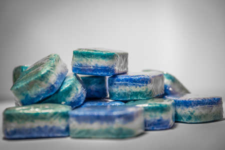 Bunch of dishwasher tablets, randomly stacked, blue, white and green colored on a white background...