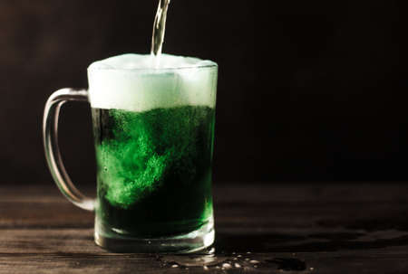 Pouring St. Patrick's green beer on a wooden surface with dark brown background