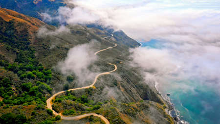 An aerial shot of beautiful green hills and a curvy road going along on the edge and amazing sea...