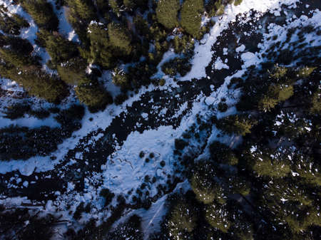 An aerial shot of a frozen river in the forest in winter