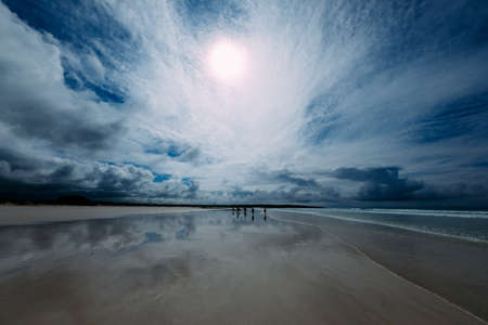 A beautiful shot of a seashore with people walking in the distance with a beautiful sky in the...