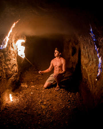 A shirtless male exploring a narrow small cage with a torch