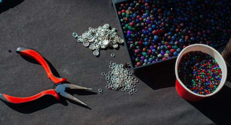 A high angle shot of the colourful beads in the container and in the cup on the black fabricの写真素材