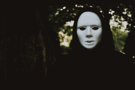 A mysterious person in a white face mask walking in the woods