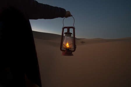 A wide shot of a person holding a lighted lantern on the background of an erg desert