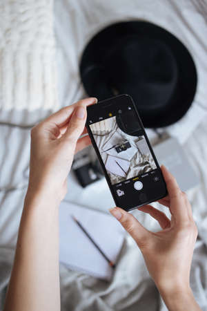 A top view of a person taking a picture of a hat, camera, and books on her mobile device