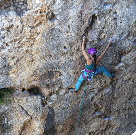 A climber woman climbing on the rocks holding from the ropes