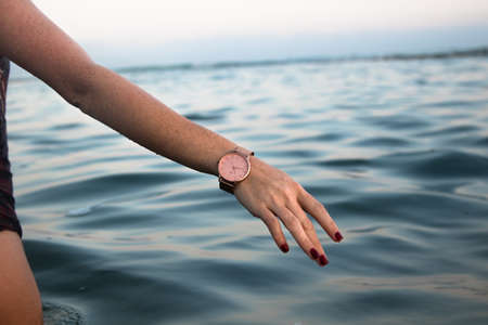 A closeup shot of a Caucasian female wearing a pink watch on her hand with freckles on the background of the seaの写真素材